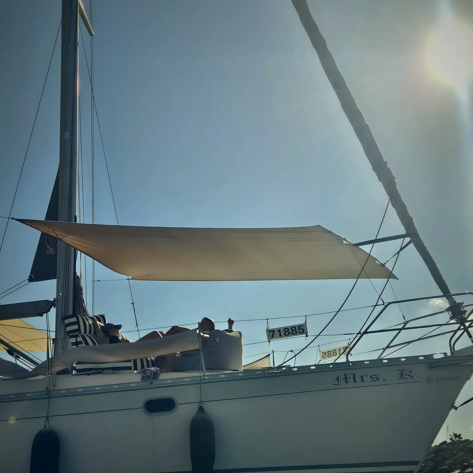 Two people lounging on the foredeck of a sailing yacht in the shade of a SunSkipper canopy